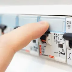 Palec naciska na wyłącznik nadprądowy w skrzynce elektrycznej.